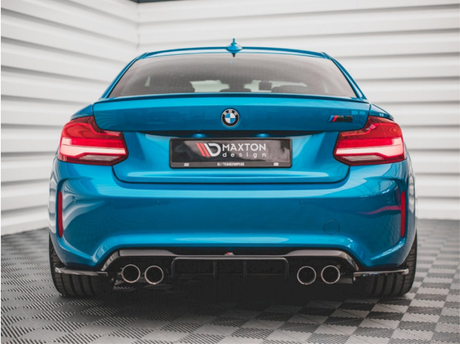 A blue BMW car is stationary, rear-facing, with dual exhausts visible. It bears the text "MAXTON design" on a plate. The background features a white, ribbed wall.