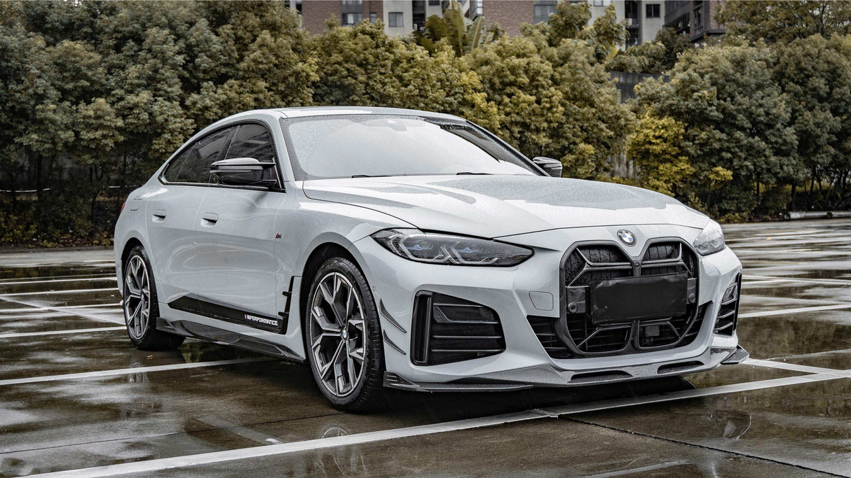 A sleek white BMW is parked on wet pavement, featured prominently in a spacious outdoor parking lot, bordered by lush green trees. Text found: "M Performance."