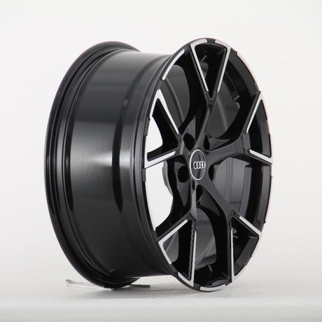 A glossy black alloy wheel with a multi-spoke design featuring a central Audi logo, stands on display against a plain white background.