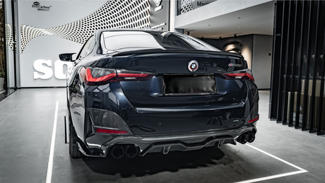 A sleek, dark-colored car is parked in a showroom with a modern design. The car's rear features prominent taillights and quad exhaust pipes. The wall has text: "wrkz DryCarbon™."
