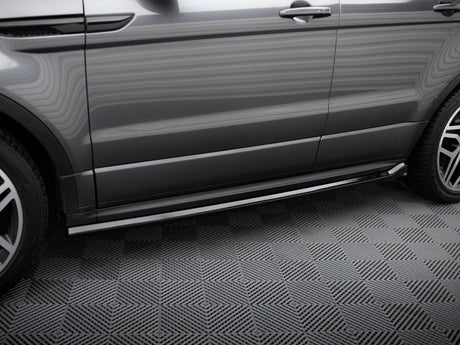 A grey SUV side, with polished metallic running boards, is parked on a patterned floor. The vehicle has clean lines and sleek wheel rims, indicating a modern design.