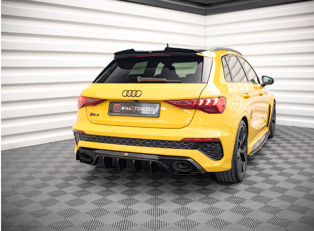 A yellow Audi RS3 is parked in a showroom with a geometric floor and white walls. The license plate reads "MATONIZED" with a social media icon.