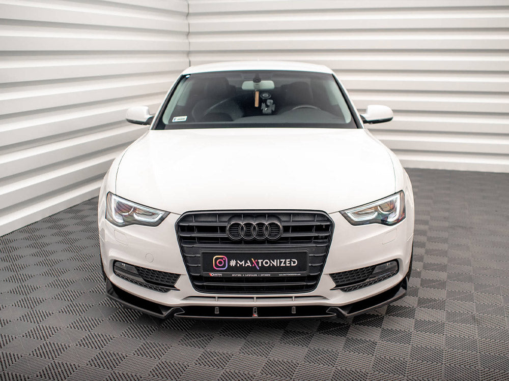 A white car faces forward in a well-lit, enclosed space with patterned flooring. Its license plate reads "INSTAGRAM #MAXTONIZED" and displays the Audi logo prominently on the grille.