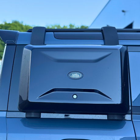 A Land Rover-branded box is mounted on a vehicle, with a clear blue sky and greenery in the background.