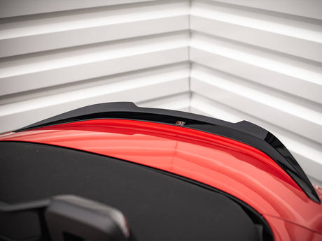 A red sports car's rear end with a black aerodynamic spoiler is parked against a textured white garage door with horizontal lines.