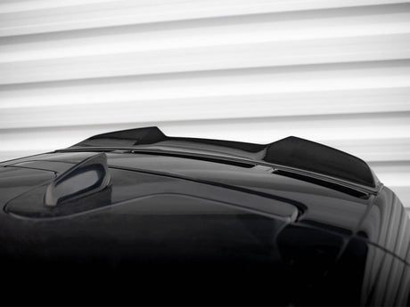 A black car roof features a shark fin antenna and two sleek air inlets. The background displays horizontal white ridges, resembling a garage door or wall paneling.