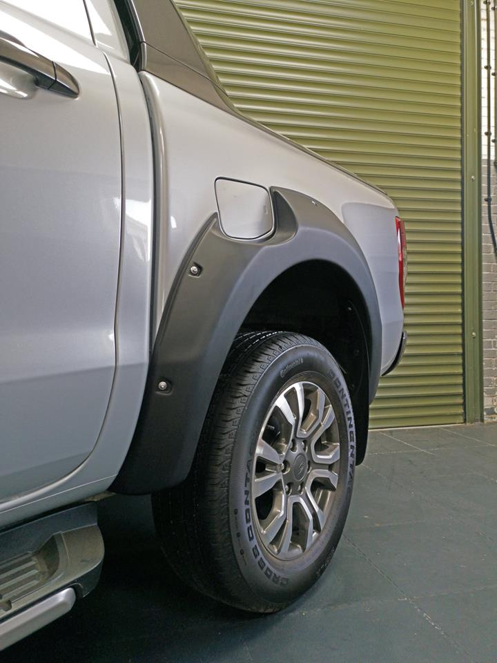 A silver pickup truck's rear wheel, equipped with a fender flare, is parked on a dark floor in front of a large, closed green garage door.