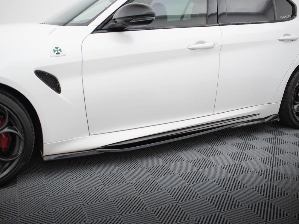 A white car is parked, showcasing its side view with a clover emblem near the front fender. It rests on a textured, patterned flooring.