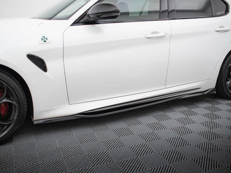 A white car is parked, showcasing its side view with a clover emblem near the front fender. It rests on a textured, patterned flooring.