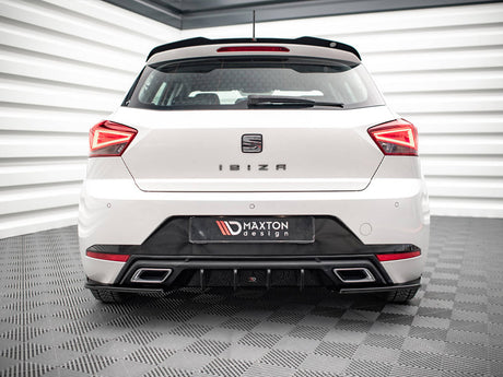 A white car is parked in a showroom. The rear features the text "IBIZA" and "MAXTON design," with distinct taillights and a sleek bumper. The room has checkered flooring.