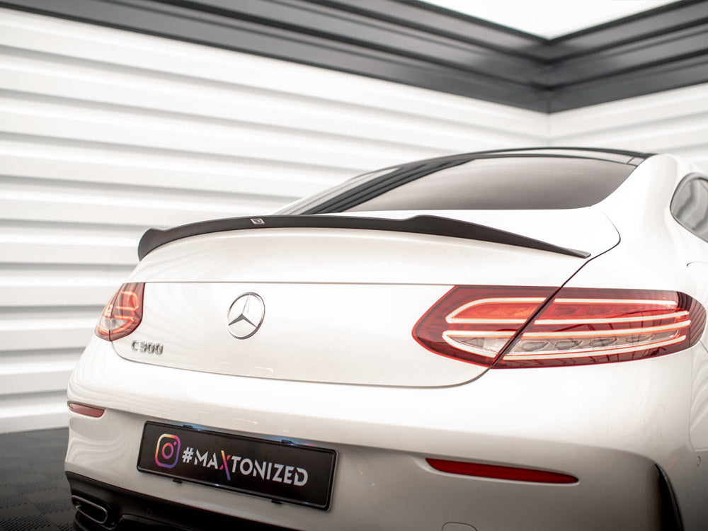 A white Mercedes-Benz C 300 is parked indoors, showcasing its rear with sleek taillights and a spoiler. The environment includes white paneled walls. The license plate reads "#MAXTONIZED".