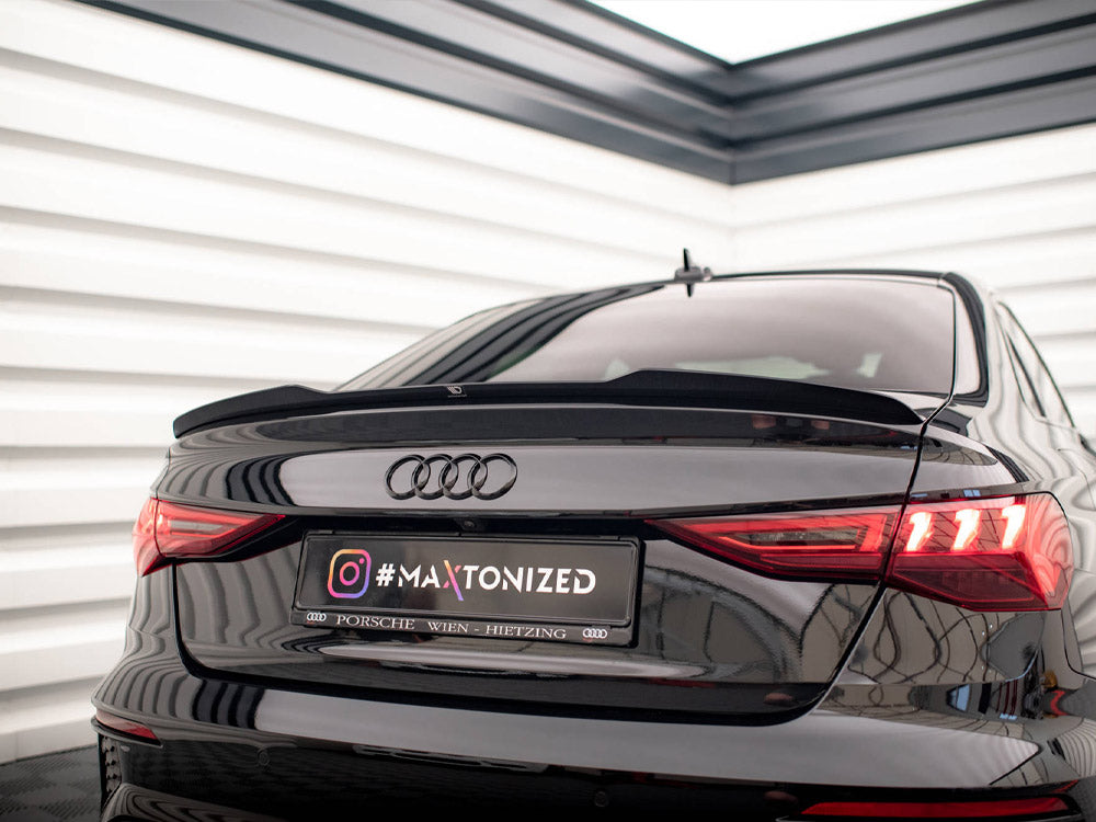 A black Audi car is parked indoors, facing away. The taillights are illuminated, and the license plate reads "#MAXTONIZED Porsche Wien Hietzing." The setting has white panel walls.