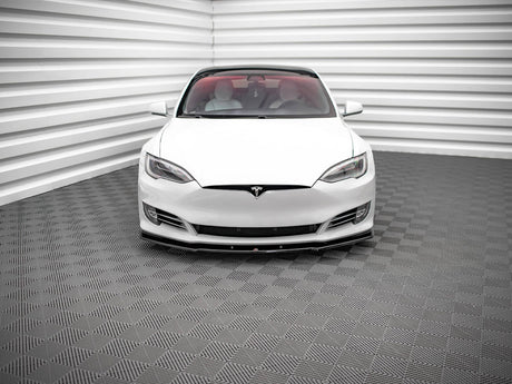 A white car, viewed from the front, is parked in a room with textured, gray-patterned flooring and walls featuring horizontal white panels.