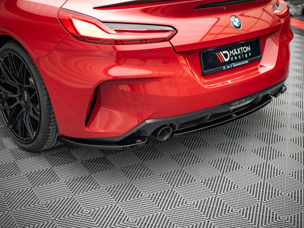 A red BMW car's rear, featuring sleek taillights and a dual exhaust, is parked on a patterned floor. The license plate reads "MAXTON design ✯ BAVARIA MOTORS."