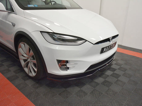 A white Tesla car is stationary, showcasing a front view on a black-and-red checkered floor. The license plate reads "MAXTON."