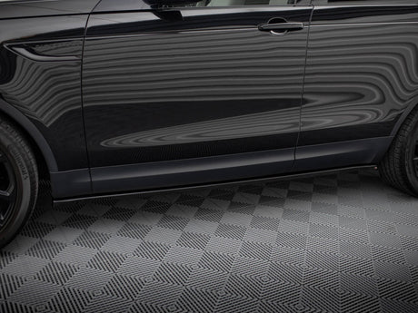 A black SUV side view shows reflections on its surface with "DISCOVERY" text near the front door. It stands parked on a textured gray floor, showcasing two tires.