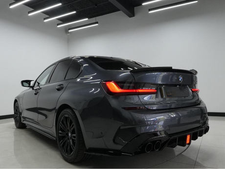 A dark gray car with tinted windows is parked in a well-lit room, showcasing sleek tail lights and a prominent rear bumper design.