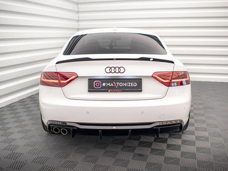 A white Audi car is stationary in a room with white, ribbed walls and checkered flooring. The rear license plate displays "#MAXTONIZED" with Instagram and Audi Sport logos.