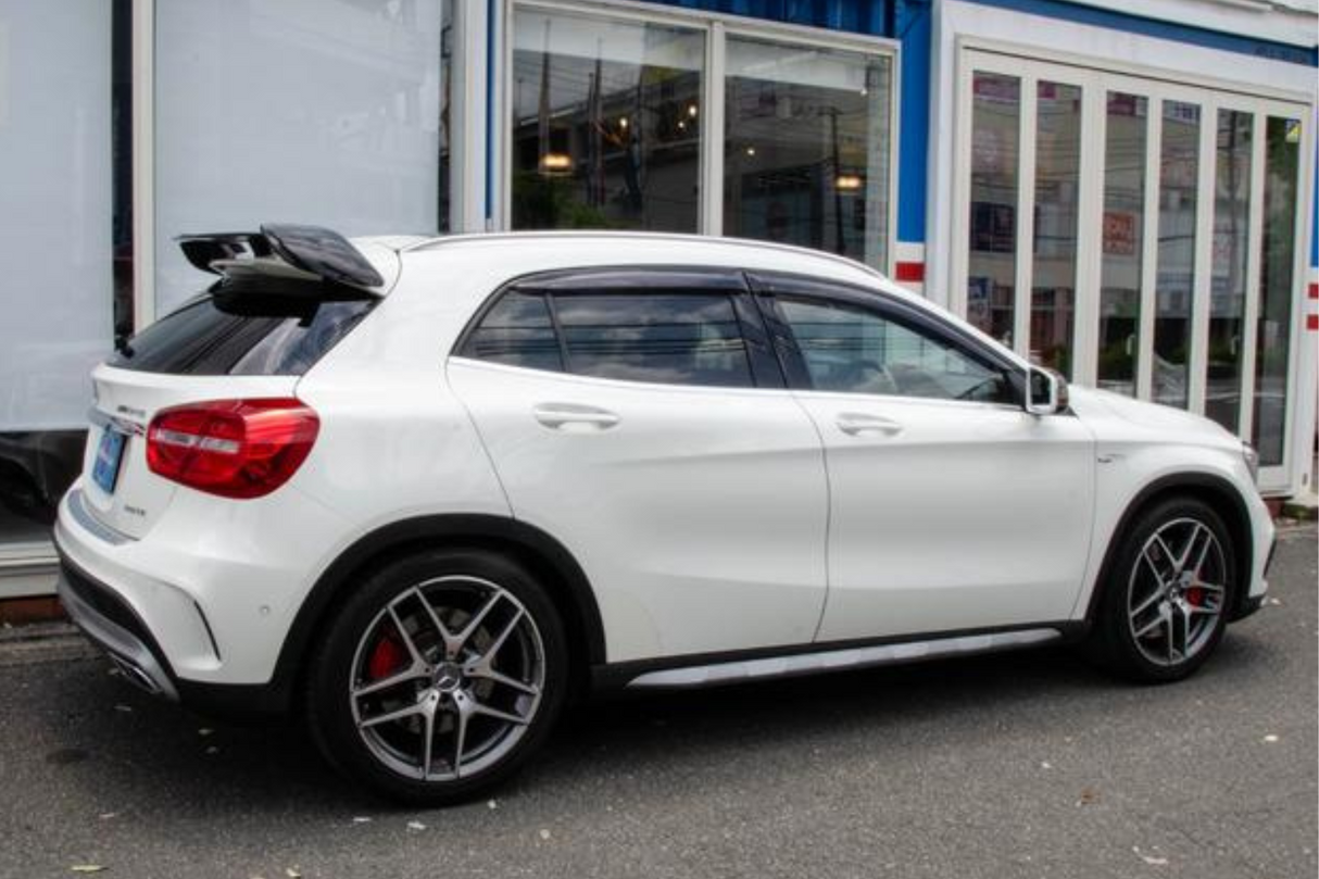 A white car with tinted windows and red brake calipers is parked on a street beside a building with large glass windows and a blue and white facade.
