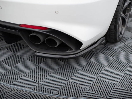 Car exhaust pipes protrude from the rear of a white vehicle, parked on a gray, textured, diamond-patterned surface, with a visible rear tire and partial red reflector.