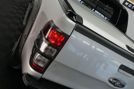 A white Ford pickup truck is parked on a black checkered floor, displaying its red and white taillights prominently. Reflections are visible on the vehicle's glossy surface.