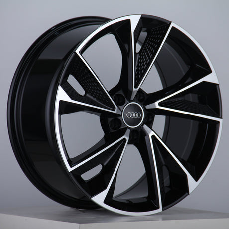 A glossy, black alloy wheel features silver accents and the Audi logo at the center, displayed on a neutral gray background with a studio setting.