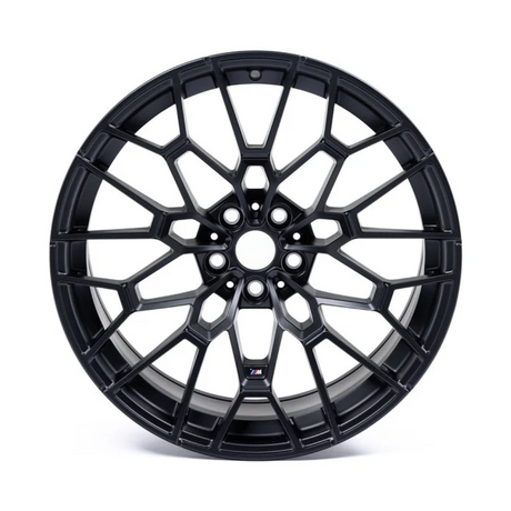 A black alloy wheel with a complex mesh design sits against a white background. The center features a small logo with blue and red stripes.