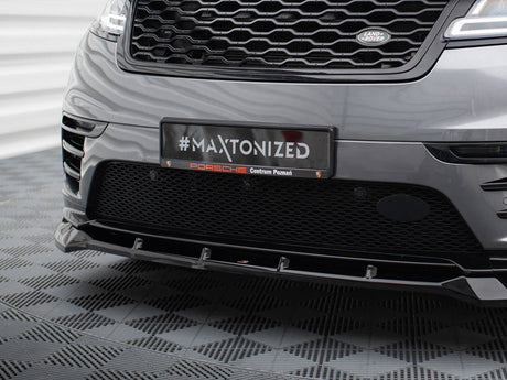 A car's front bumper with a grille displays a plaque reading "#MAXTONIZED Porsche Centrum Poznań" in a patterned indoor setting.