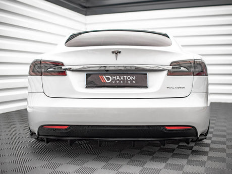 A white Tesla car is parked indoors on a textured floor, with "DUAL MOTOR" on the right and a "MAXTON design" plate in the center.