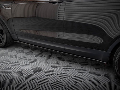 A black car rests on a geometric-patterned floor, reflecting striped wall patterns across its shiny side surface in an enclosed environment.