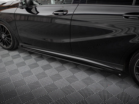 A sleek black car is parked on a geometric-patterned, gray floor. The car has tinted windows and black alloy wheels, reflecting a striped ceiling above.