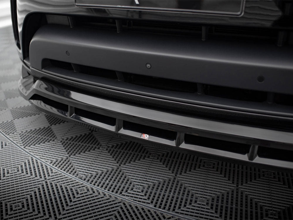 A black car's front bumper with a sleek design is shown in detail, featuring a small "3D" logo. It rests on a geometric-patterned mat.