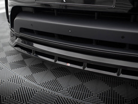 A black car's front bumper with a sleek design is shown in detail, featuring a small "3D" logo. It rests on a geometric-patterned mat.