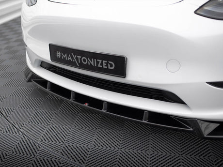 A car's front bumper, displaying a hashtag "#MAXTONIZED" on a black license plate, is shown on a textured gray patterned floor in an indoor setting.