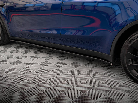A blue car with sleek, reflective bodywork, parked on a textured geometric-patterned floor, shows partial view of a wheel and door on the right side.