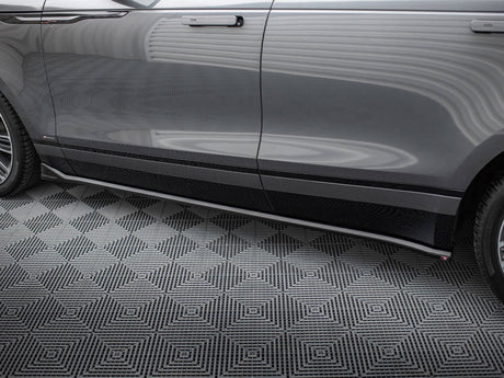 A shiny gray car door with sleek side mirror and wheel, parked on a geometric-patterned black and gray floor in a well-lit garage.