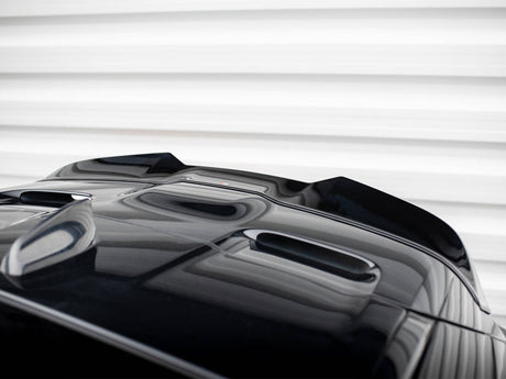 A glossy black car's hood with streamlined air vents sits stationary, reflecting light. It's positioned against a backdrop of horizontal, white, textured panels.