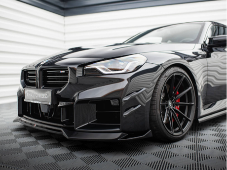 A sleek black sports car with a low front bumper and red-accented wheels is parked on a patterned floor against a backdrop of horizontal white and black lines.