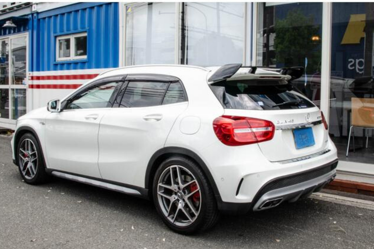 White car parked beside a blue shipping container building, displaying shiny rims and tinted windows. The background includes glass doors and a building interior with chairs.