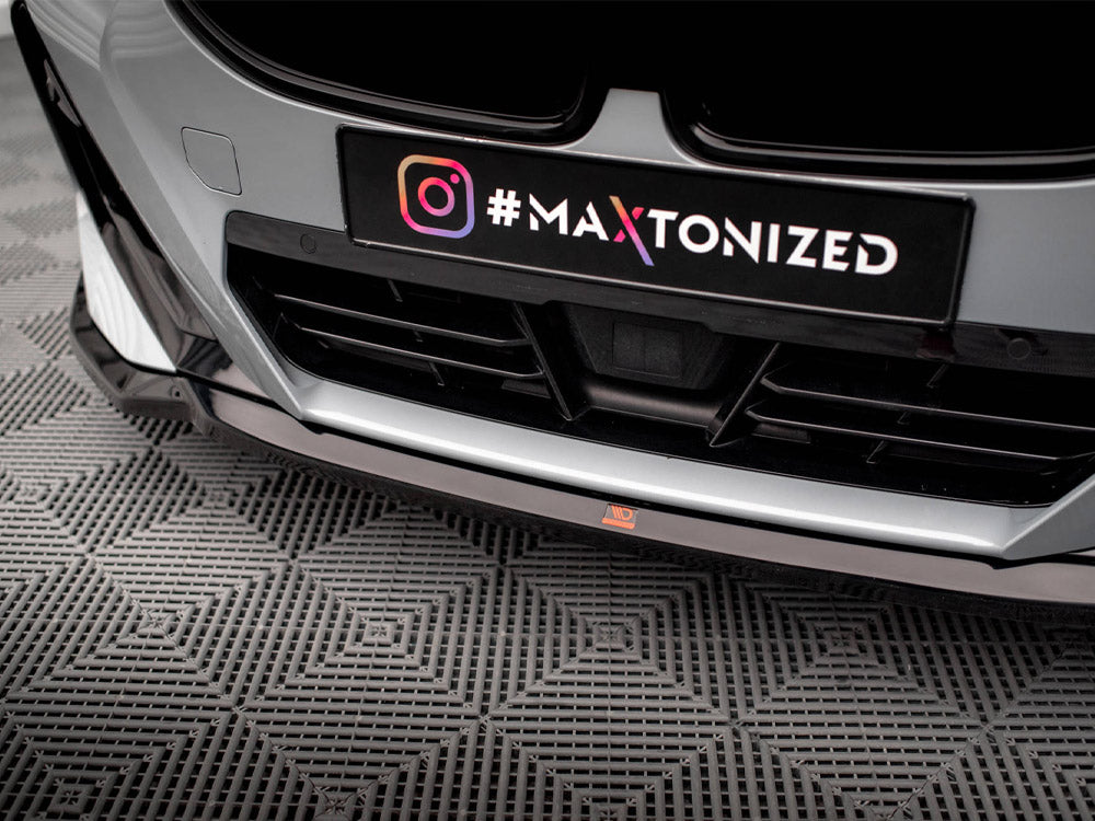 Car front bumper with a sleek design features a black license plate displaying an Instagram logo and the text "#MAXTONIZED." It is situated on a textured, patterned floor.