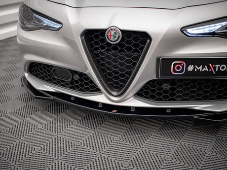 A silver car's front bumper with a hexagonal grille, prominent logo, and illuminated headlights, parked on a patterned floor. Text: "#MAXTO" and Instagram logo.
