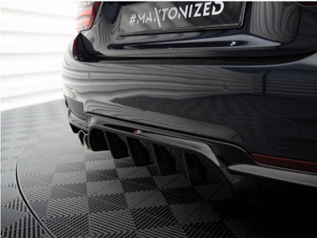 A car's rear bumper features a #MAXTONIZED license plate and quad exhaust pipes, set in a garage with a textured floor pattern and reflective panels.