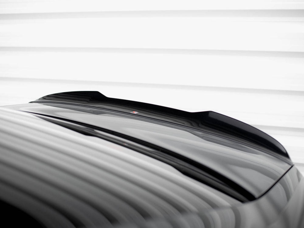 A glossy black car roof with a subtle spoiler reflects light, under a white striped ceiling, creating a sleek, modern appearance.