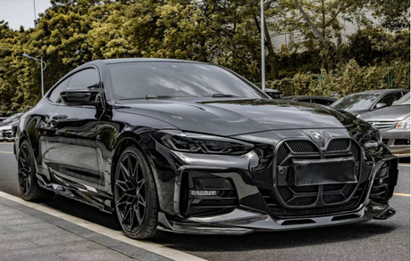 A sleek black sports car is parked on a street lined with trees and other vehicles, its glossy surface reflecting the surroundings, emphasizing its modern, aerodynamic design.