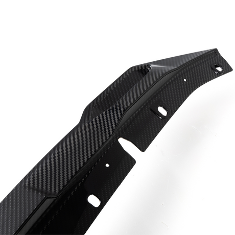A contoured carbon fiber car part with multiple holes lies against a white background, showcasing a sleek, textured design often used for aerodynamic enhancements.