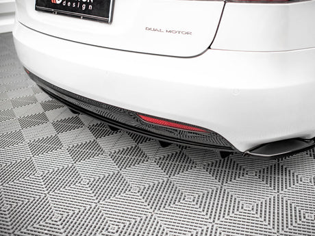 A white car's rear, labeled "DUAL MOTOR," is parked on a gray, textured floor. A red reflector is visible on the lower bumper, and the license plate includes "design."