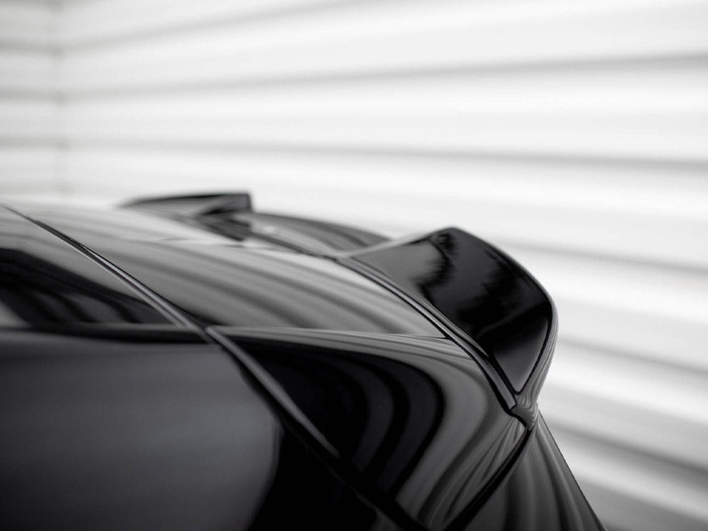 A sleek, black car spoiler is shown from a low angle; the surface reflects light. The background is a blurred, white, horizontal-striped wall.