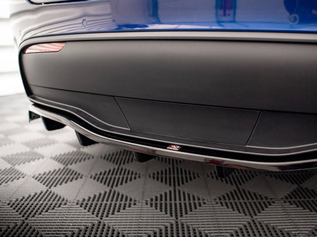 A blue car's rear bumper features a sleek aerodynamic design with a diffuser. A small "ADRO" logo is visible. The car is on a checkered pattern floor, likely in a showroom.