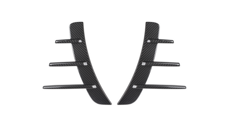 Two black carbon fiber pieces with three horizontal fins each are symmetrically aligned. They are set against a plain white background, suggesting automotive parts.