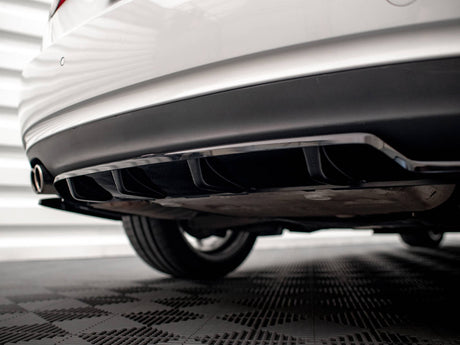 The rear of a white car with a black diffuser and dual exhaust pipes is parked on a checkered floor, against a backdrop of horizontal white panels.